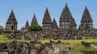 a large stone building with grass in front of a church with Prambanan in the background jigsaw puzzle